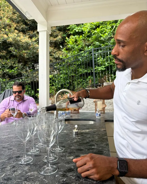 Manuel Patterson pouring white wine into a row of glasses at an outdoor bar