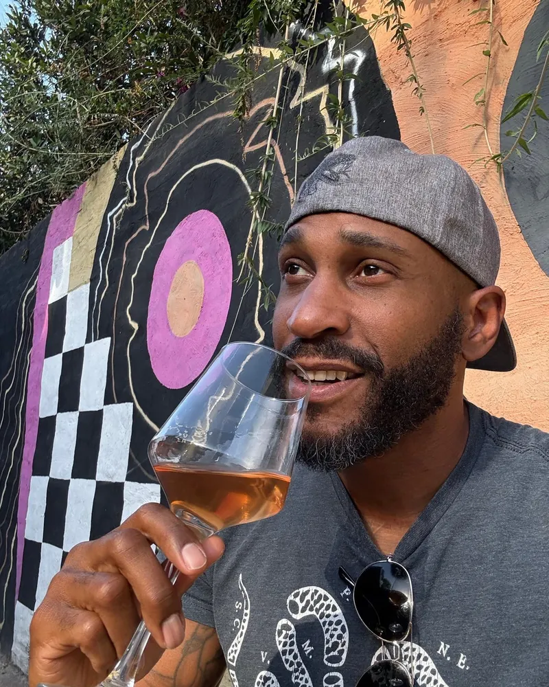 Manuel Patterson tasting a glass of rosé in front of a colorful street mural