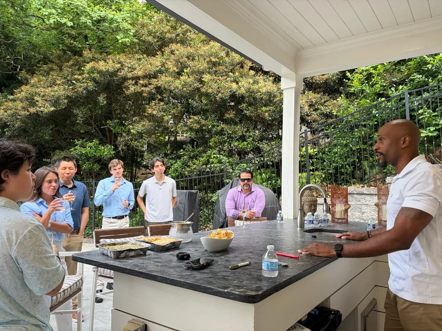 A group of guests holding wine glasses and listening to Manuel Patterson on a covered patio