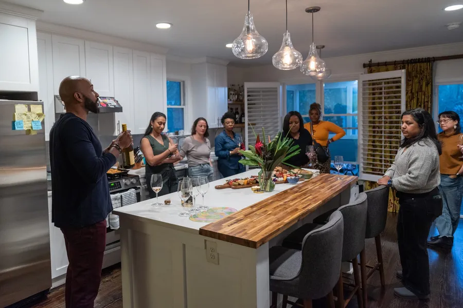 Manuel Patterson presenting a wine to guests standing around a kitchen island
