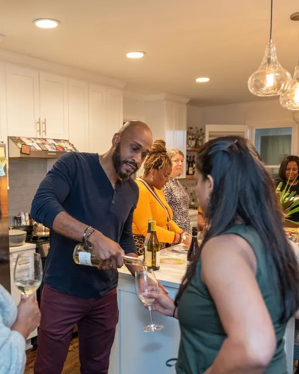 Manuel Patterson pouring white wine for guests holding glasses in a home kitchen