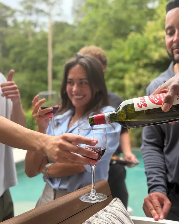 Red wine being poured into a glass held by a smiling guest beside a pool
