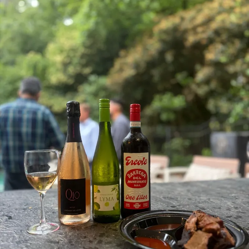 Three bottles of wine lined up on a stone counter with a glass of white wine and a snack plate